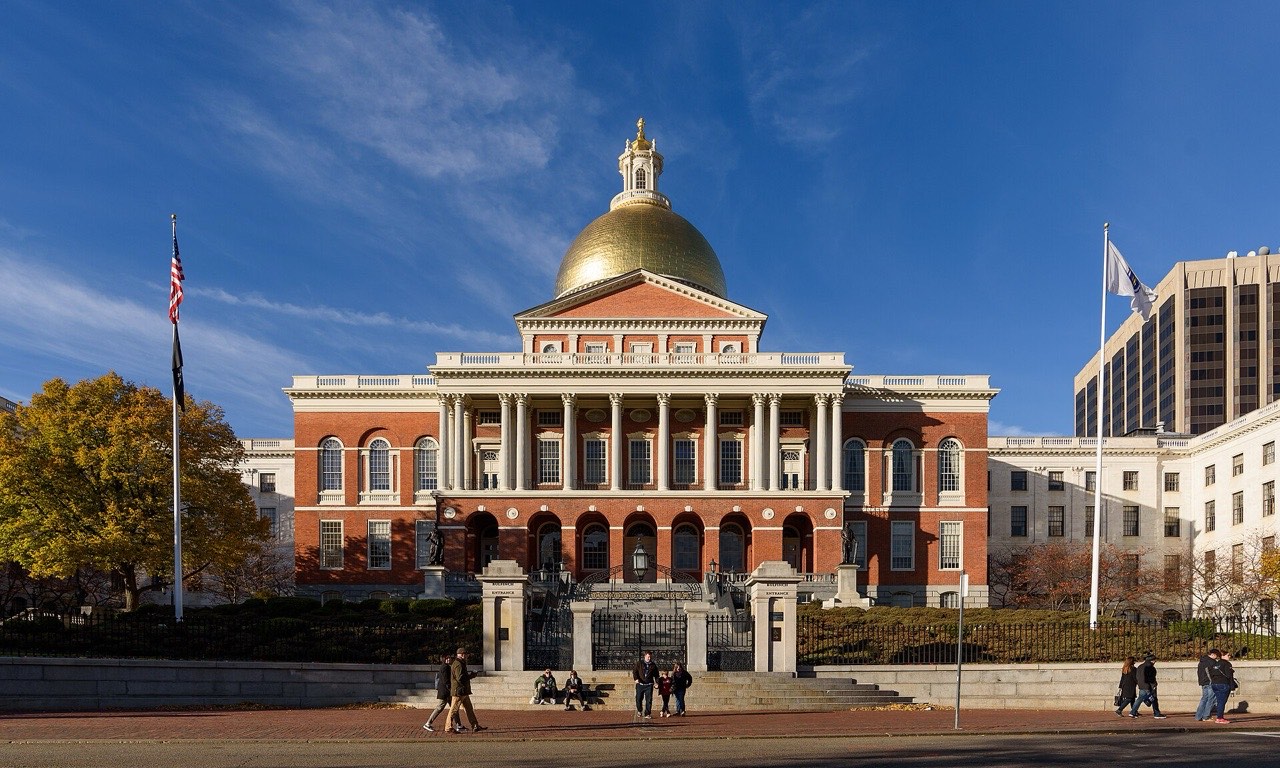 Red-brick Massachusetts State House with gold dome and white columns in Boston under a blue autumn sky
