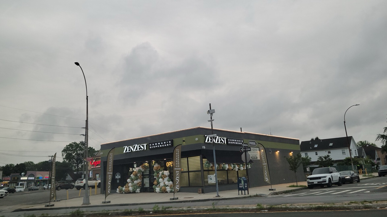 Corner storefront of a licensed cannabis dispensary in Queens with opening-day balloons under a gray sky